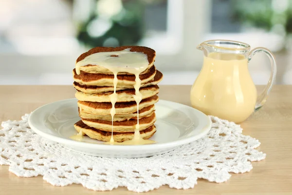Zoete pannenkoeken op plaat met gecondenseerde melk op tafel in de keuken — Stockfoto