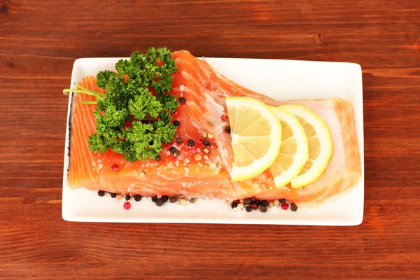 Fresh salmon fillet with herbals and lemon slices on plate, on wooden background — Stock Photo, Image