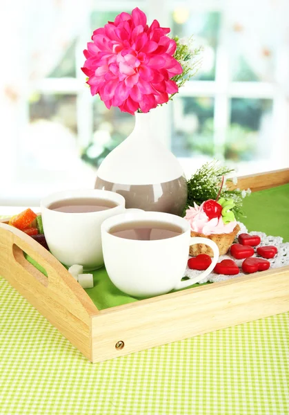 Cups of tea with flower and cake on wooden tray on table in room — Stock Photo, Image