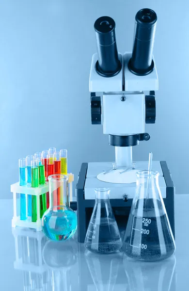 Test tubes with colorful liquids and microscope in blue light — Stock Photo, Image