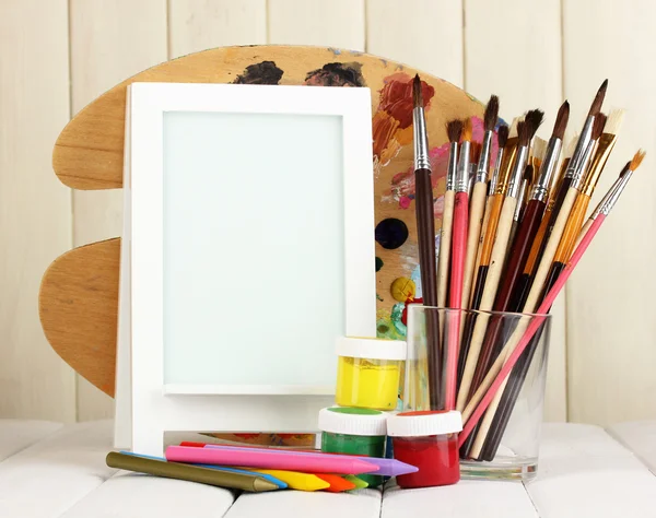 Photo frame as easel with artist's tools on wooden background — Stock Photo, Image