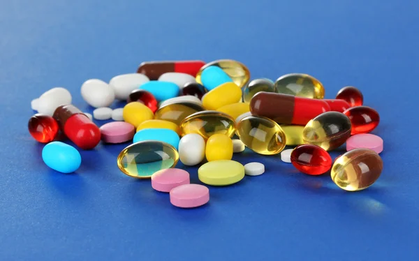 Surtido de pastillas, tabletas y cápsulas sobre fondo azul — Foto de Stock