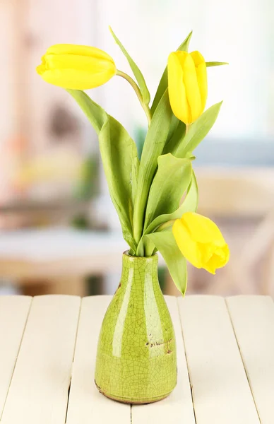 Žluté tulipány ve váze na dřevěný stůl na pozadí místnosti — Stock fotografie