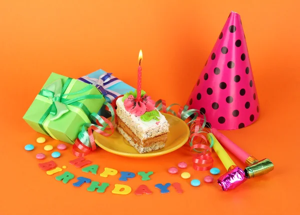 Bolo de aniversário colorido com vela e presentes no fundo laranja — Fotografia de Stock