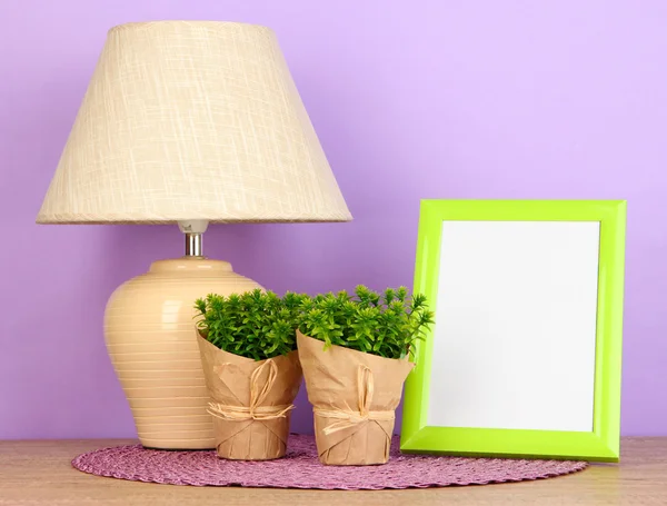 Colorful photo frame, lamp and flowers on wooden table on lilac background — Stock Photo, Image