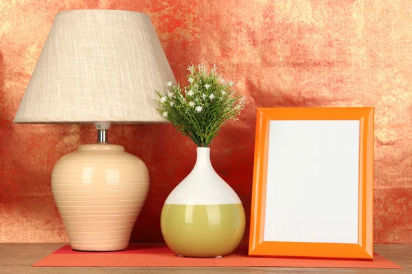 Marco de fotos colorido, lámpara y flores en la mesa de madera sobre fondo rojo — Foto de Stock