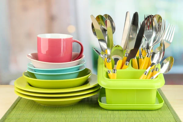 Plates, forks, knives, spoons and other kitchen utensil on bamboo mat, on bright background