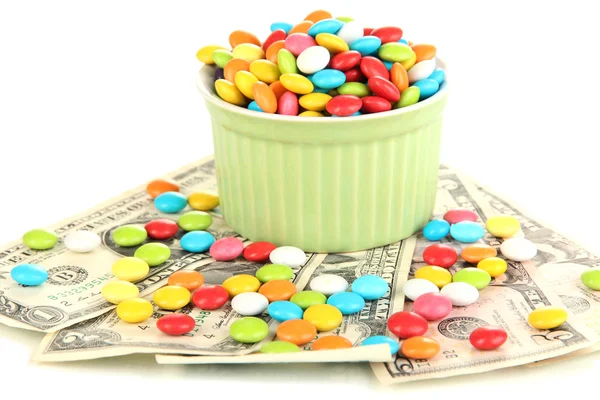 Cuenco con caramelos de colores de pie en billetes de dólar aislados en blanco —  Fotos de Stock
