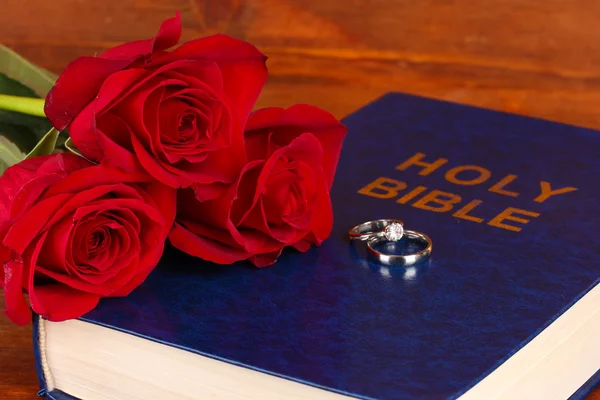 Anéis de casamento na Bíblia com rosas no fundo de madeira — Fotografia de Stock