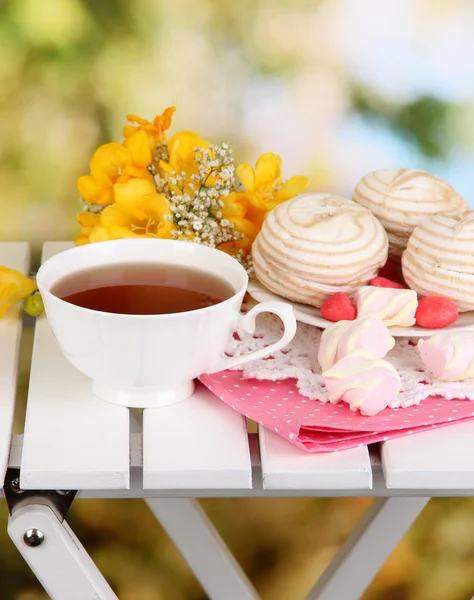 Beautiful composition with cup of tea and marshmallow on wooden picnic table on natural background — Stock Photo, Image