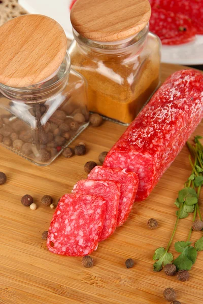 Sabroso salami en el plato y el tablero en la mesa de madera de cerca —  Fotos de Stock