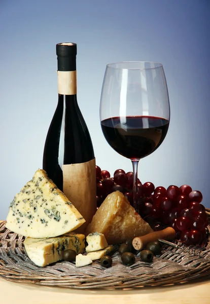 Natura morta raffinata di vino, formaggio e uva su vassoio di vimini su tavolo di legno su sfondo blu — Foto Stock