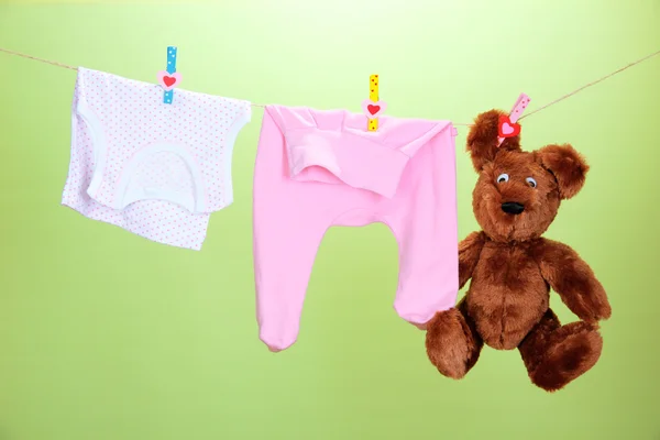 Vêtements de bébé suspendus sur corde à linge, sur fond de couleur — Photo