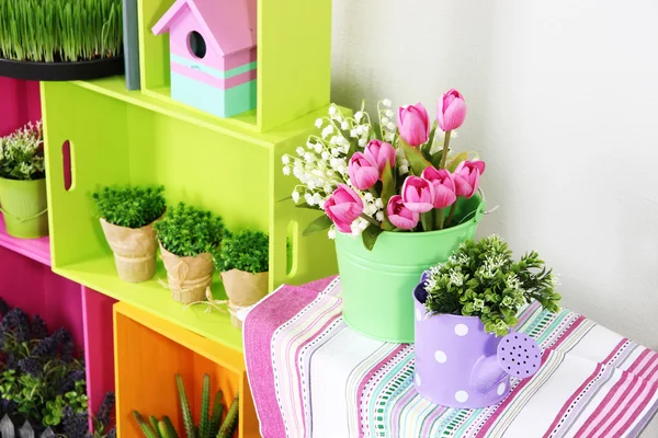 Estantes coloridos y mesa con elementos decorativos y flores —  Fotos de Stock