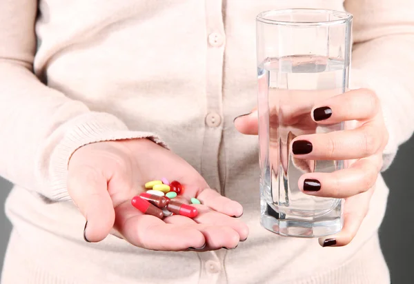 Muchas píldoras y agua de vidrio en la mano — Foto de Stock