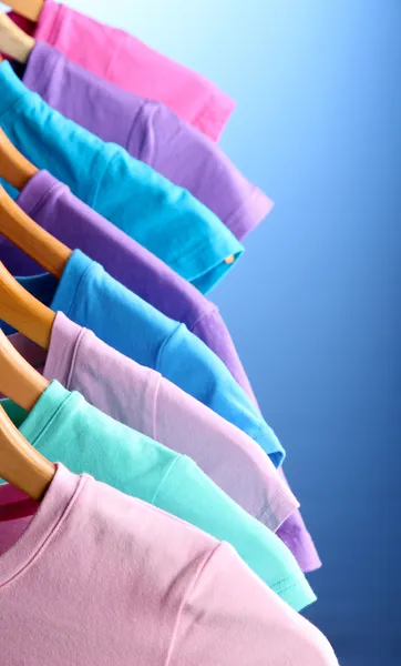Viele T-Shirts auf Kleiderbügeln auf blauem Hintergrund — Stockfoto