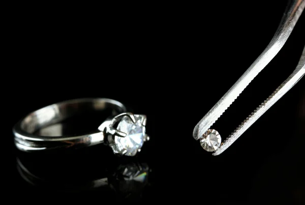 Shining crystal (diamond) in the tweezers and ring, on black background — Stock Photo, Image