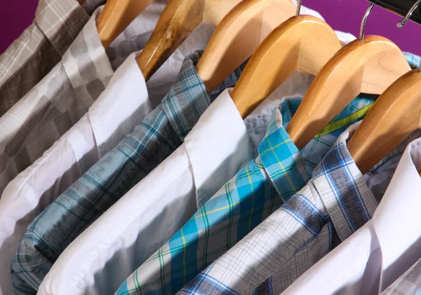 Camisas masculinas em cabides no fundo roxo — Fotografia de Stock
