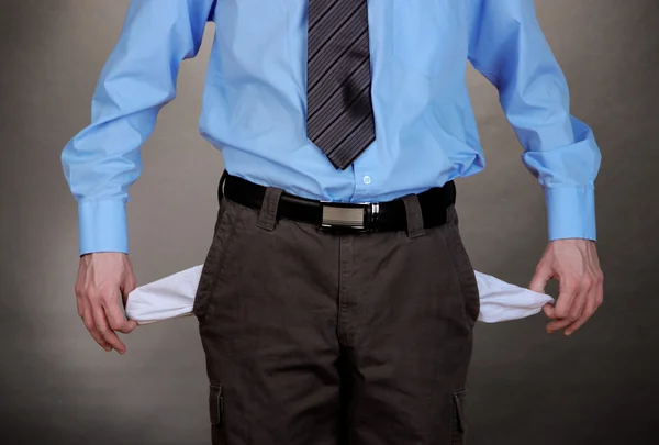 Business man showing his empty pockets, on grey background — Stock Photo, Image