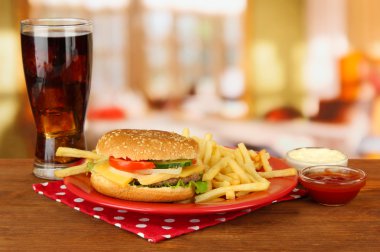 Tasty cheeseburger with fried potatoes and cold drink, on bright background clipart