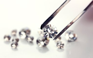 Beautiful shining crystal (diamond) in the tweezers, isolated on white