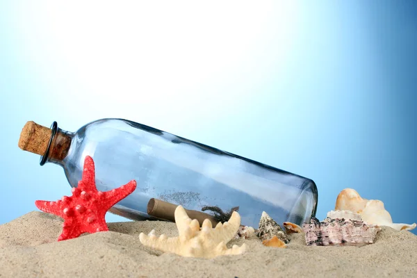 Botella de vidrio con nota interior sobre arena, sobre fondo azul —  Fotos de Stock