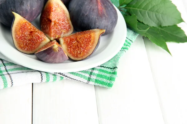 Ripe sweet figs with leaves on plate, on wooden table — Stock Photo, Image