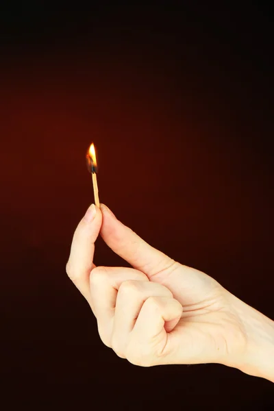 Brennendes Streichholz in weiblicher Hand, auf dunkelbraunem Hintergrund — Stockfoto