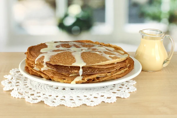 Sweet pancakes on plate with condensed milk on table in kitchen — Stock Photo, Image