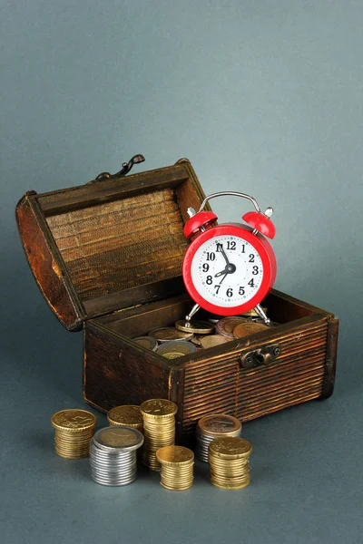 Relógio despertador com moedas no peito em fundo cinza — Fotografia de Stock