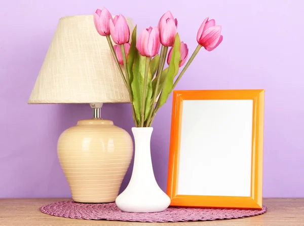 カラフルな写真フレーム、ランプ、薄紫色の背景に木製のテーブルの花 — ストック写真