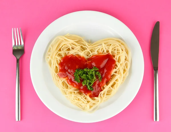 Dikkatli bir şekilde kalp şeklinde düzenlenmiş ve renkli arka plan üzerinde domates soslu tepesinde pişmiş spagetti — Stok fotoğraf