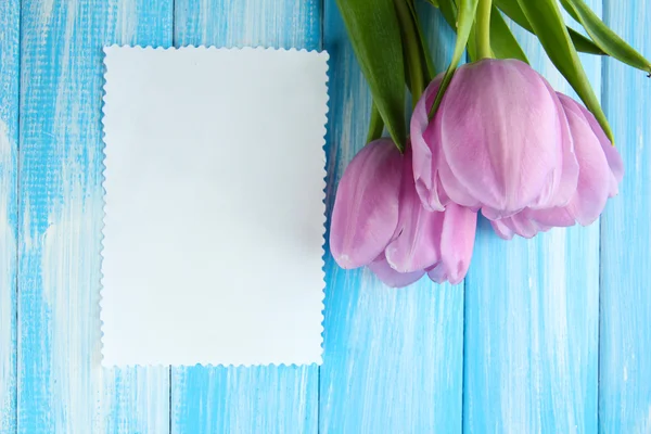 Hermoso ramo de tulipanes morados y tarjeta en blanco sobre fondo de madera azul —  Fotos de Stock