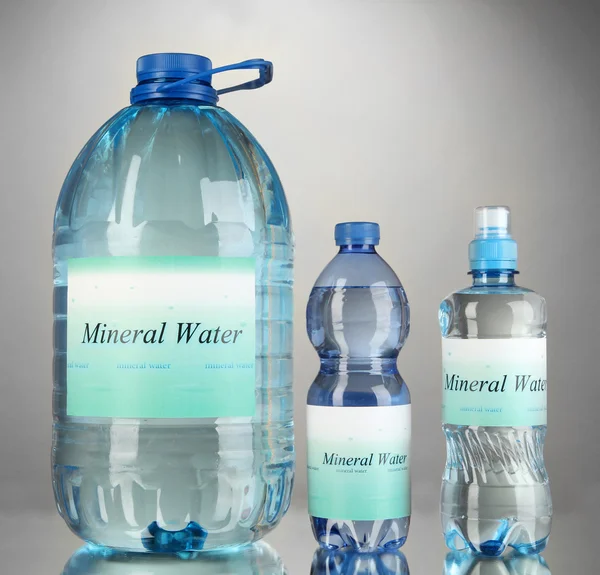 Different water bottles with label on grey background — Stock Photo, Image