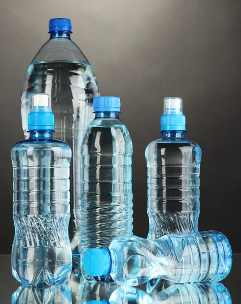 Diferentes garrafas de água no fundo cinza — Fotografia de Stock