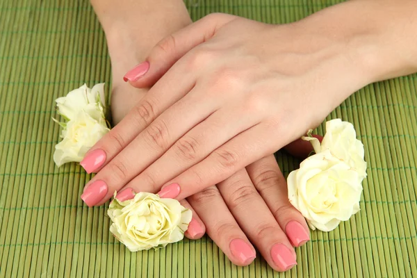 Mãos de mulher com manicure rosa e flores, em fundo tapete de bambu — Fotografia de Stock