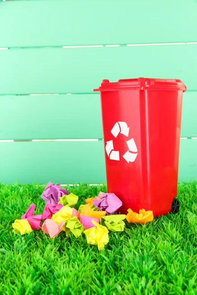 Papelera de reciclaje con papeles sobre hierba sobre fondo azul claro —  Fotos de Stock