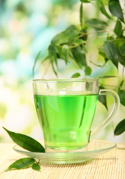 Tasse transparente de thé vert sur tapis de bambou, sur fond de nature — Photo