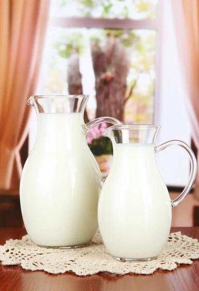 Pitchers of milk on table in room — Stock Photo, Image