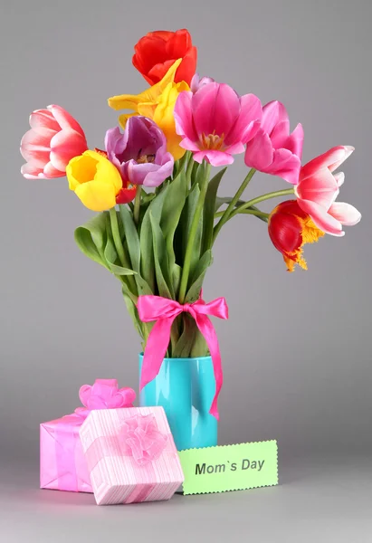 Beautiful tulips in bouquet with gifts and note on gray background — Stock Photo, Image