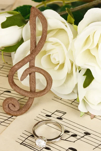 Treble clef, rozen en trouwring op muzikale achtergrond — Stockfoto