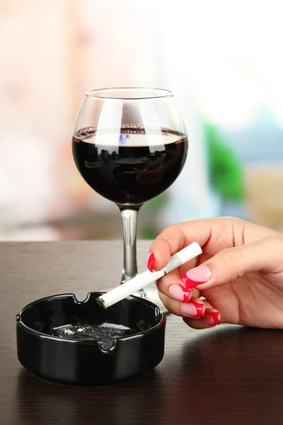 Mano femenina con copa de vino tinto y cigarrillo, sobre fondo brillante — Foto de Stock