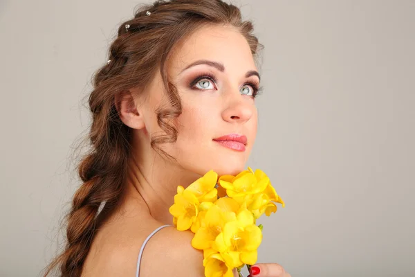 Jovem com belo penteado e flores, em fundo cinza — Fotografia de Stock