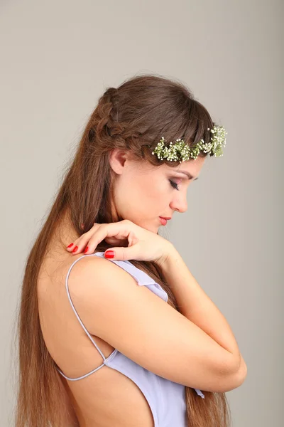 Ung kvinna med vackra frisyr och krans på grå bakgrund — Stockfoto