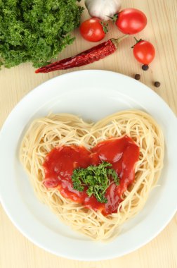 Cooked spaghetti carefully arranged in heart shape and topped with tomato sauce, on wooden background