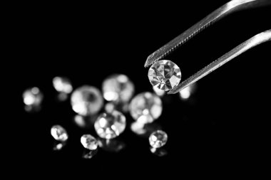 Beautiful shining crystal (diamond) in the tweezers, on black background clipart