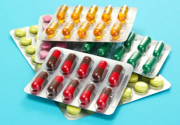 Cápsulas y pastillas empaquetadas en ampollas, sobre fondo azul — Foto de Stock
