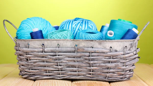 Bright threads in basket on wooden table on green background — Stock Photo, Image