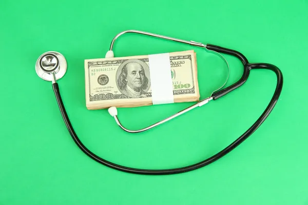 Concetto di costo sanitario: stetoscopio e dollari su sfondo verde — Foto Stock
