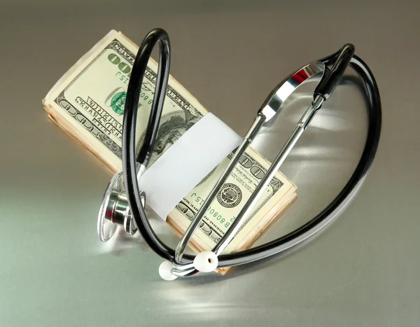 Концепция затрат на здравоохранение: стетоскоп и доллары на сером фоне — стоковое фото